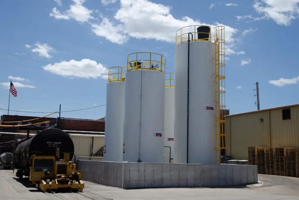 A industrial area with three white tanks and a yellow ladder going up the side of them.