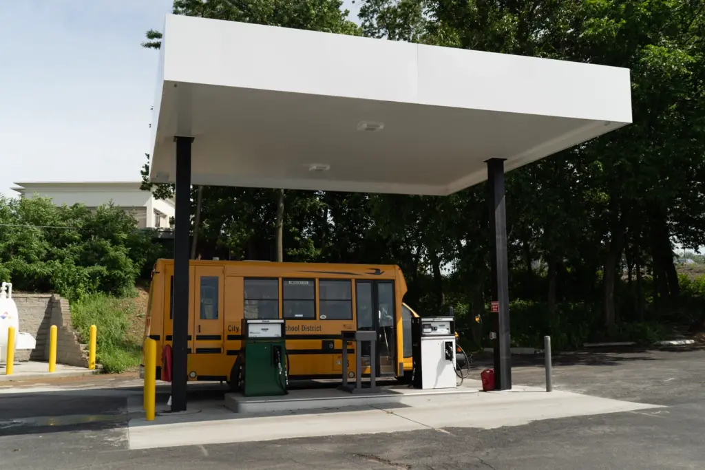 A small school bus at a gas station pump.