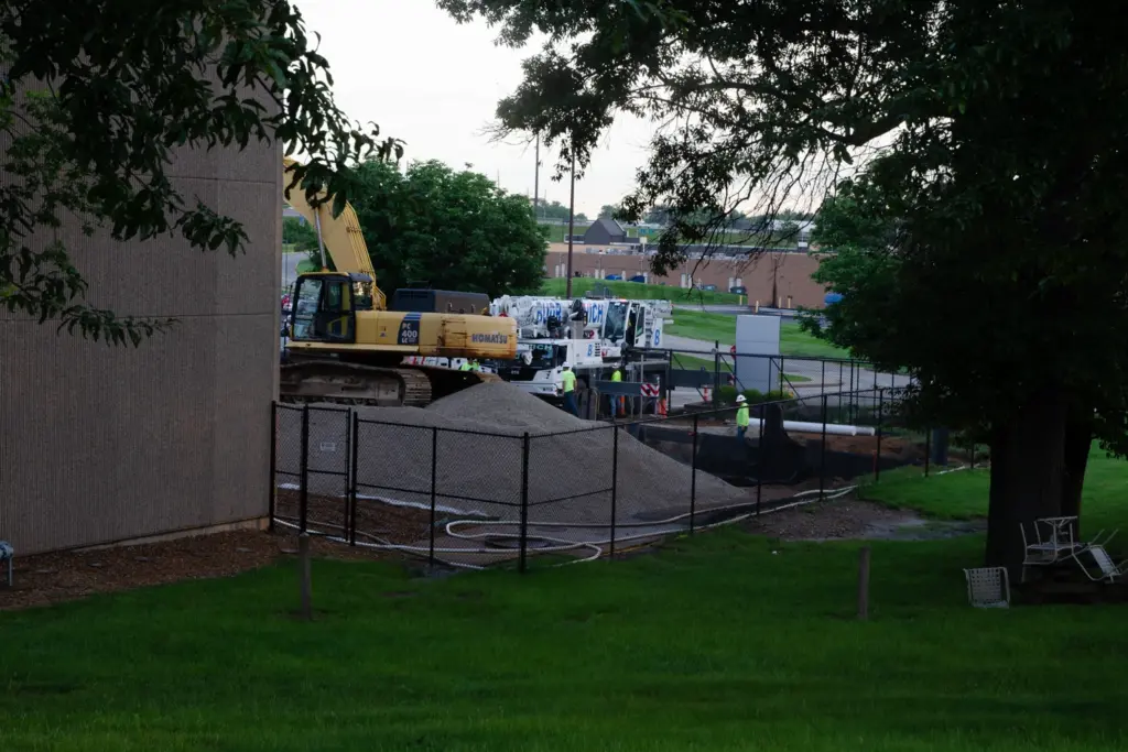 Fenced in area with a mound of rock with a bulldozer in the background.