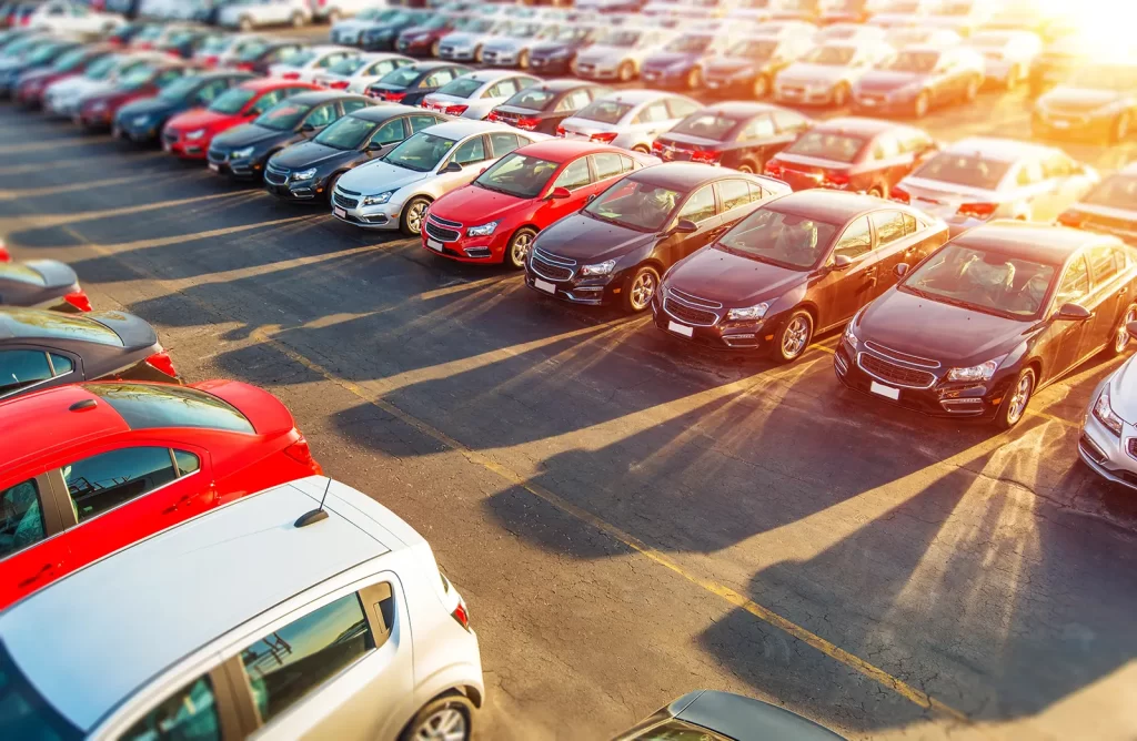 New cars aligned on a dealership lot with reflective sun rays.